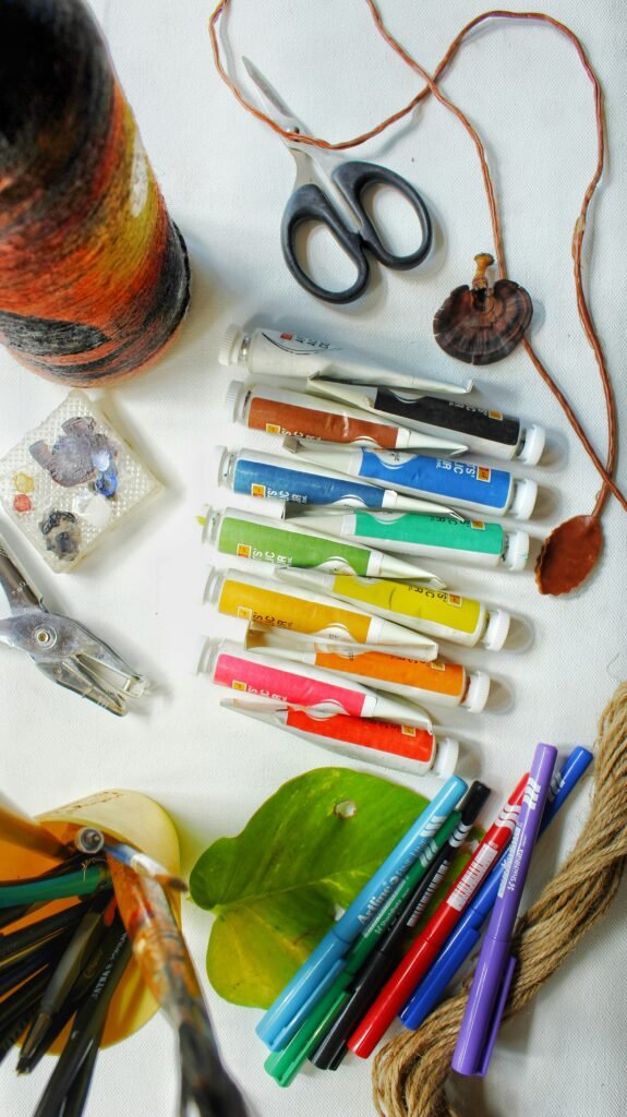 Flatlay of craft supplies including paint tubes, markers, scissors and brushes