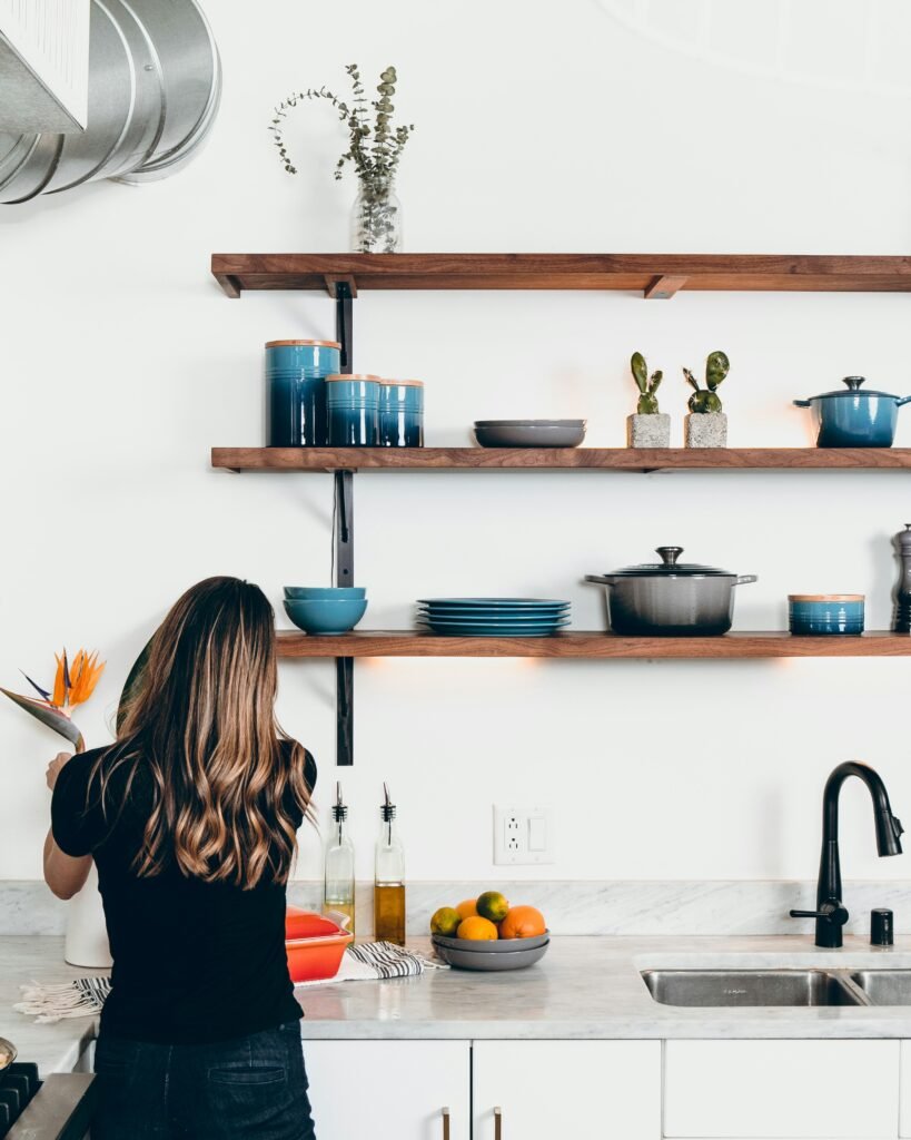 Woman arranging flowers in a bright kitchen with neat open wooden shelves