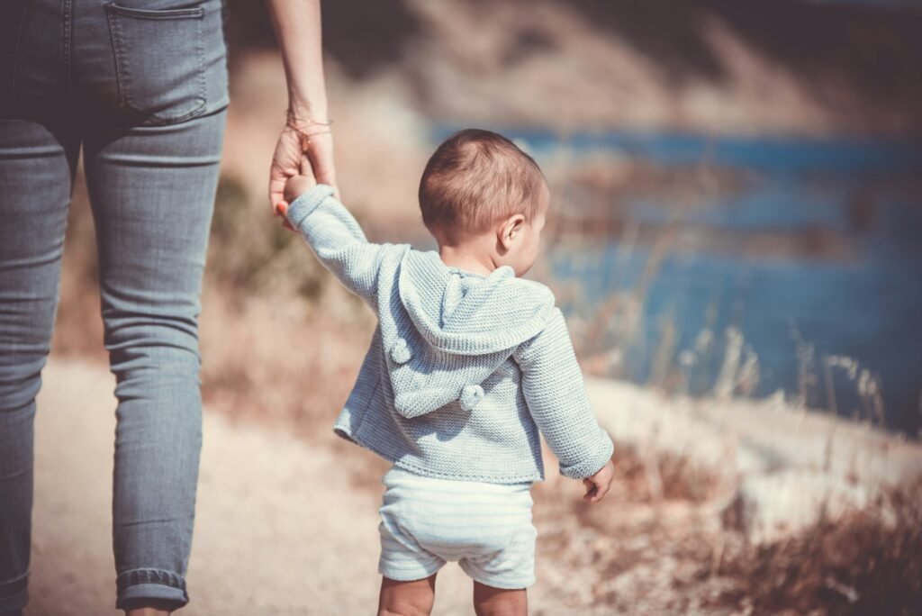 Mother holding her toddler's hand on a walk beside the wate