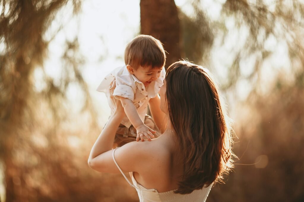 Mother joyfully lifting her baby into the air in warm golden evening light