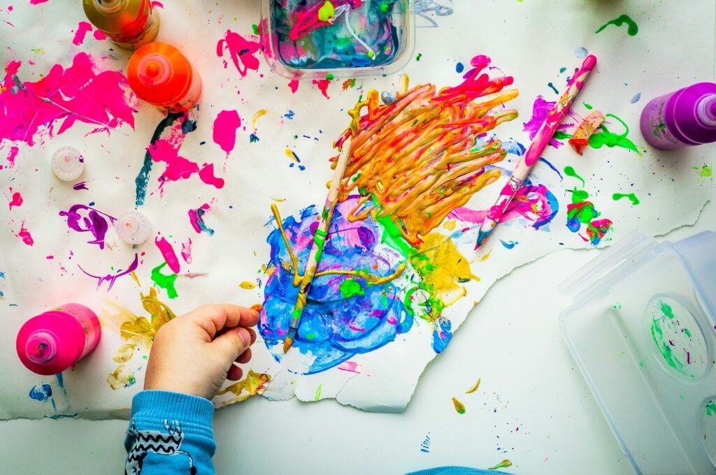 Child's hand painting colourful messy artwork with bright paints on paper