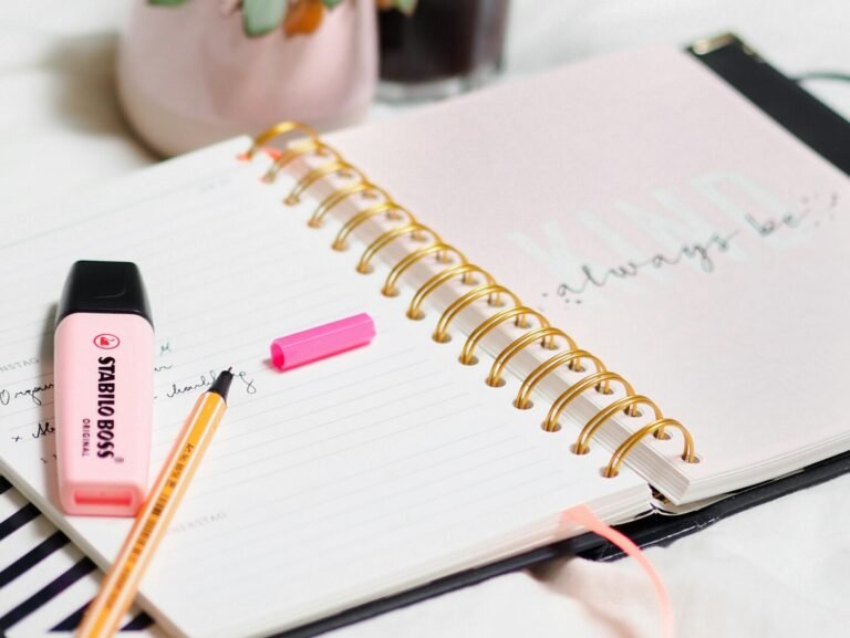 A spiral notebook with highlighters, a plant and iced coffee