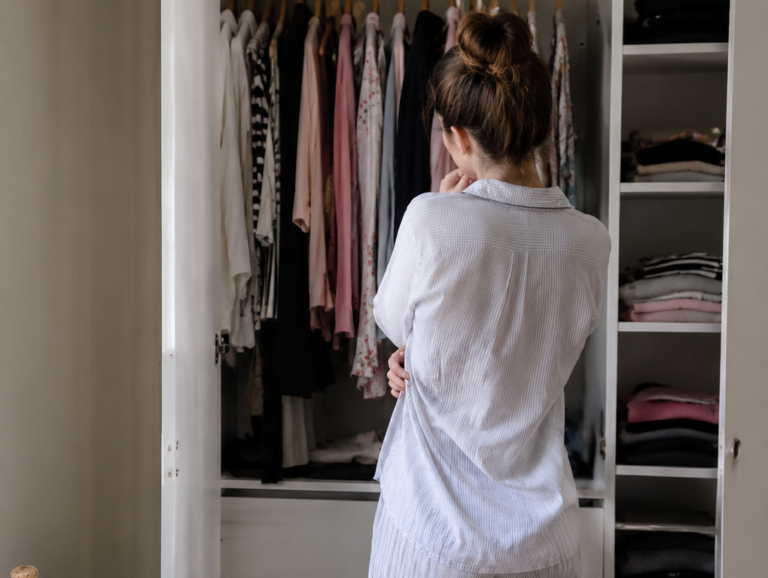 Woman in pajamas at a neatly organized white wardrobe of folded and hung clothes, easing the ADHD morning routine
